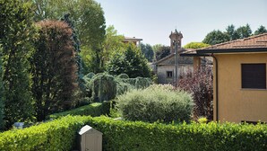 A garden with a wooden shed, a yellow building, and a church with a bell tower.