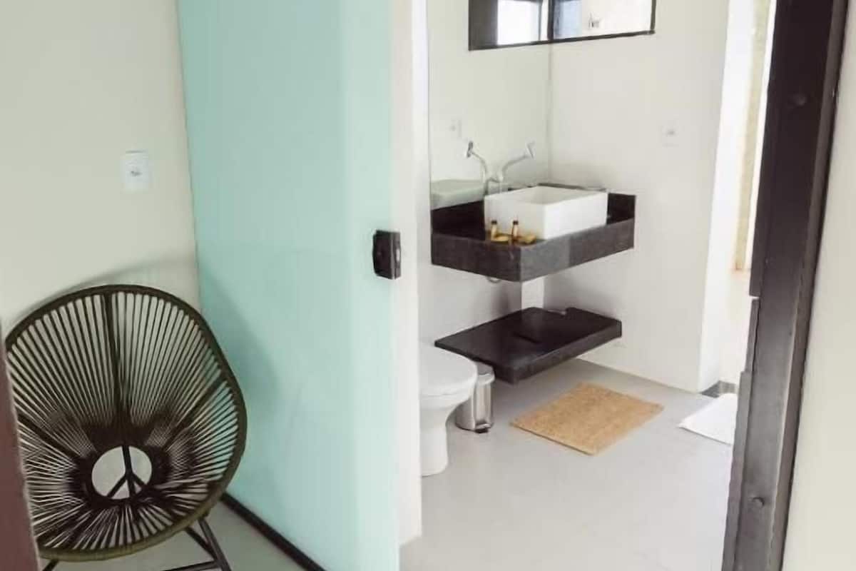 A modern bathroom with a white sink, a mirror, and a black chair.