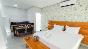 Habitació d'hotel amb llit de fusta, roba de llit blanca, taula de fusta petita, cuina americana i un mur amb un disseny decoratiu.