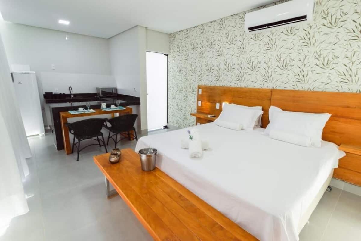 A hotel room with a wooden bed, white linens, a small wooden table, a kitchenette, and a patterned wall.