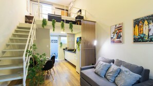Un espace de vie moderne comprenant un escalier, un canapé gris agrémenté de coussins à motifs, un coin repas et une cuisine.