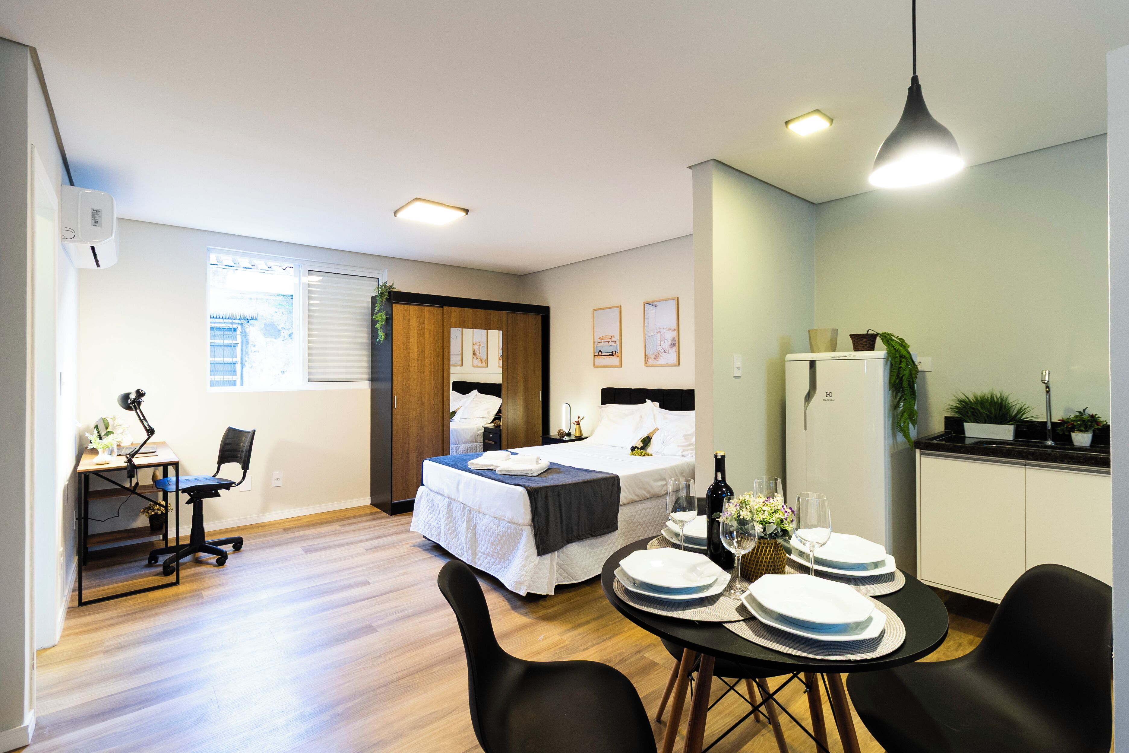 A hotel room with a bed, desk, dining table, chairs, and a kitchenette.