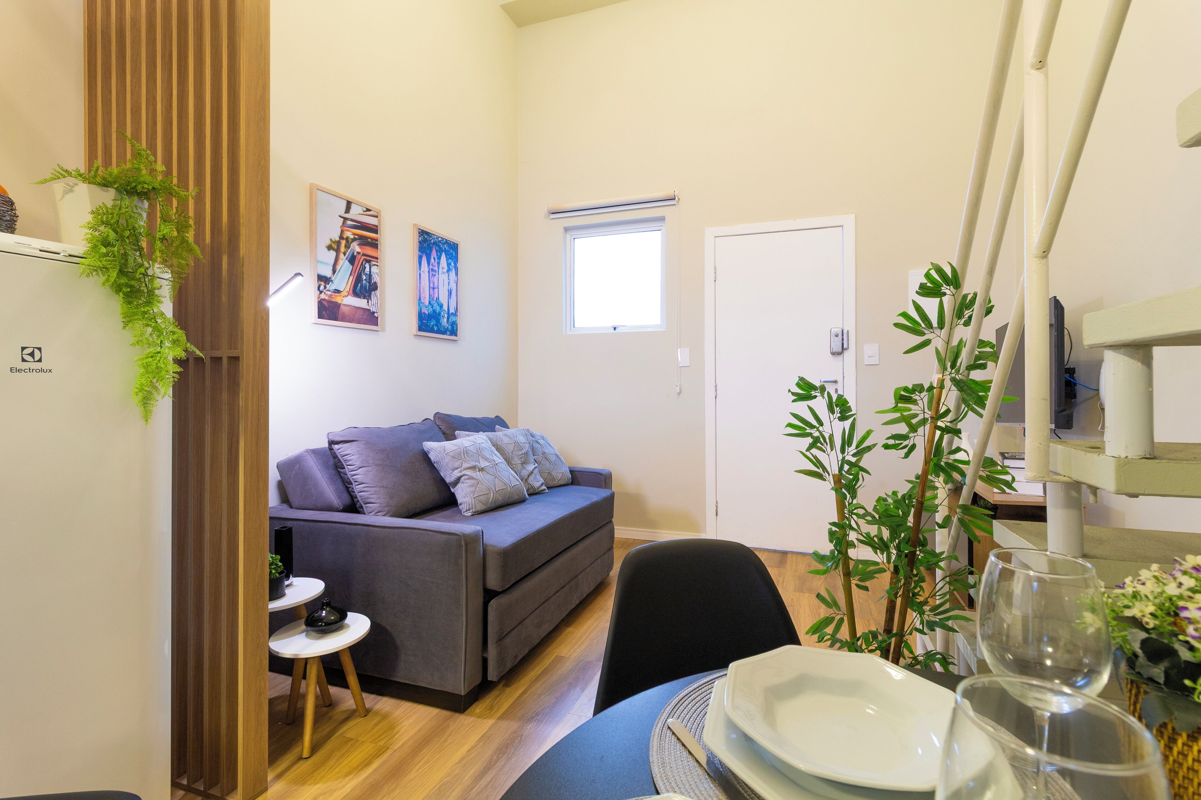 Un espacio habitable pequeño con un sofá, una mesa de comedor dispuesta con platos y vasos, una mesita auxiliar y una ventana.