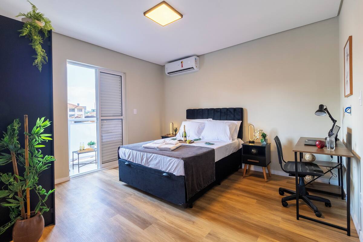 Een slaapkamer met een bed, bureau, stoel en potplanten.