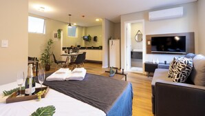 Une chambre d’hôtel moderne avec un lit, une télévision, un coin repas et une cuisine en arrière-plan.