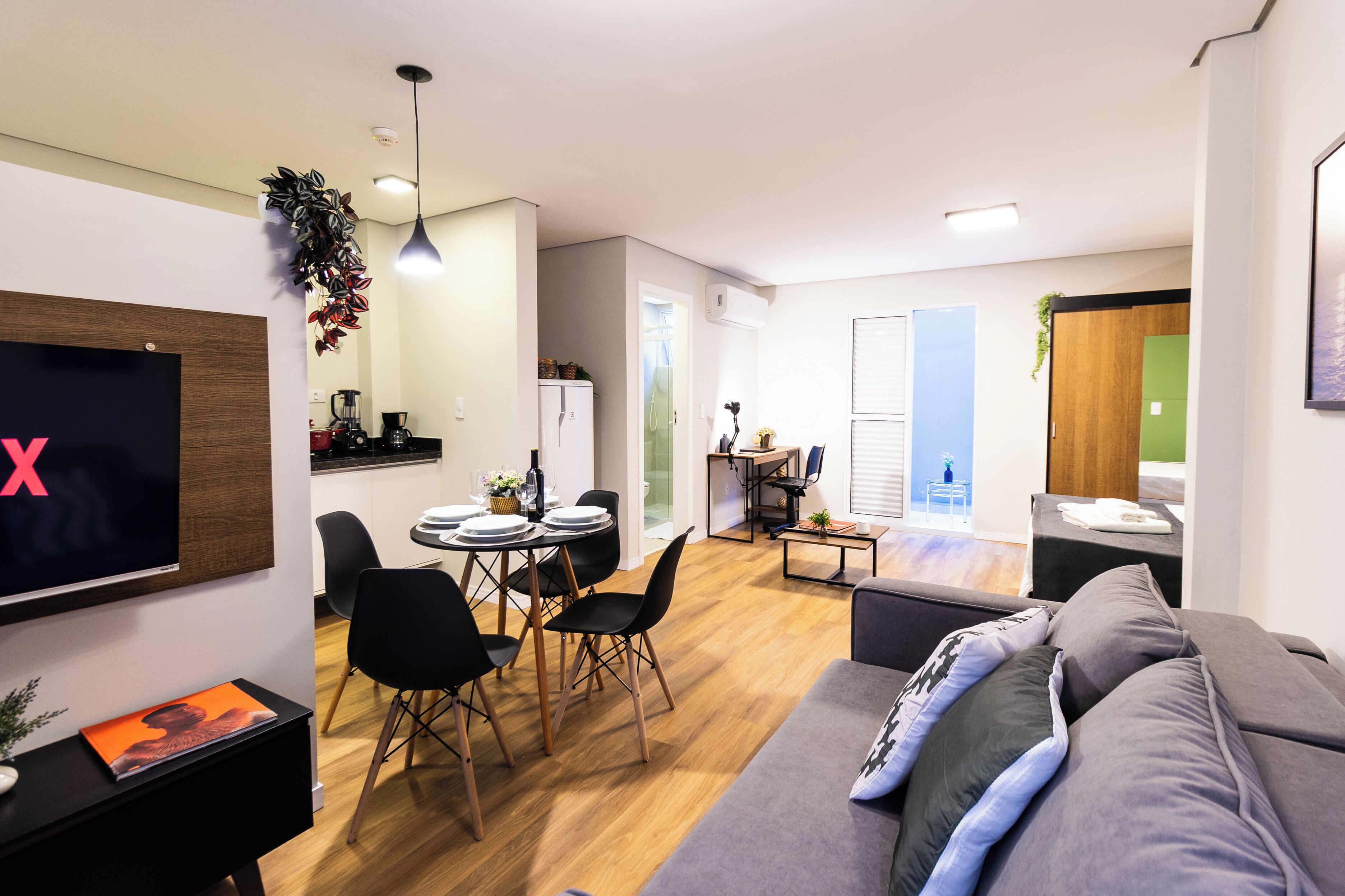 Ein modernes Wohnzimmer mit einem grauen Sofa, schwarzen Sesseln, einem Esstisch und einem Fernseher.