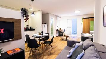 Ein modernes Wohnzimmer mit einem grauen Sofa, schwarzen Sesseln, einem Esstisch und einem Fernseher.