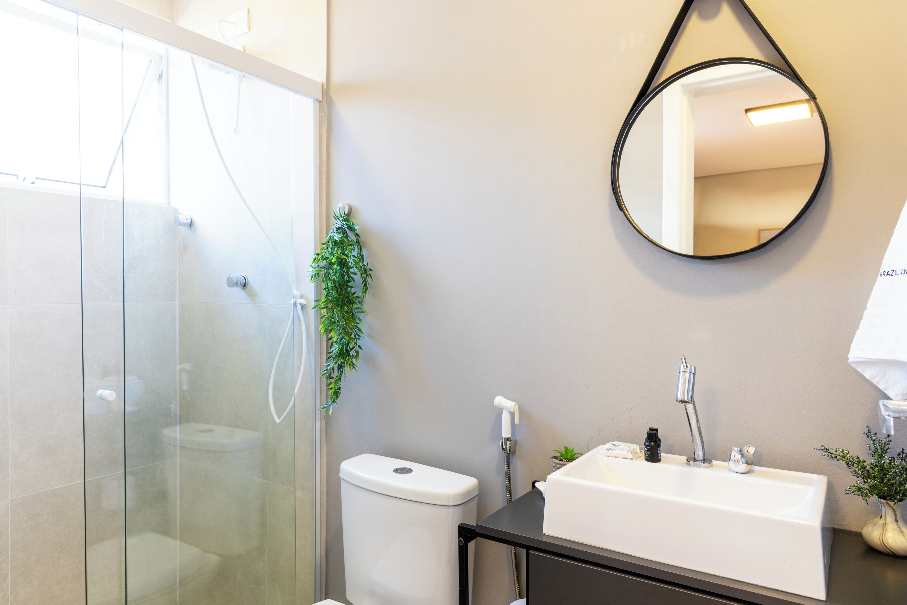 A modern bathroom with a glass-enclosed shower, a white toilet, a black sink with a mirror, and a small potted plant.