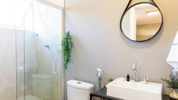 A modern bathroom with a glass-enclosed shower, a white toilet, a black sink with a mirror, and a small potted plant.