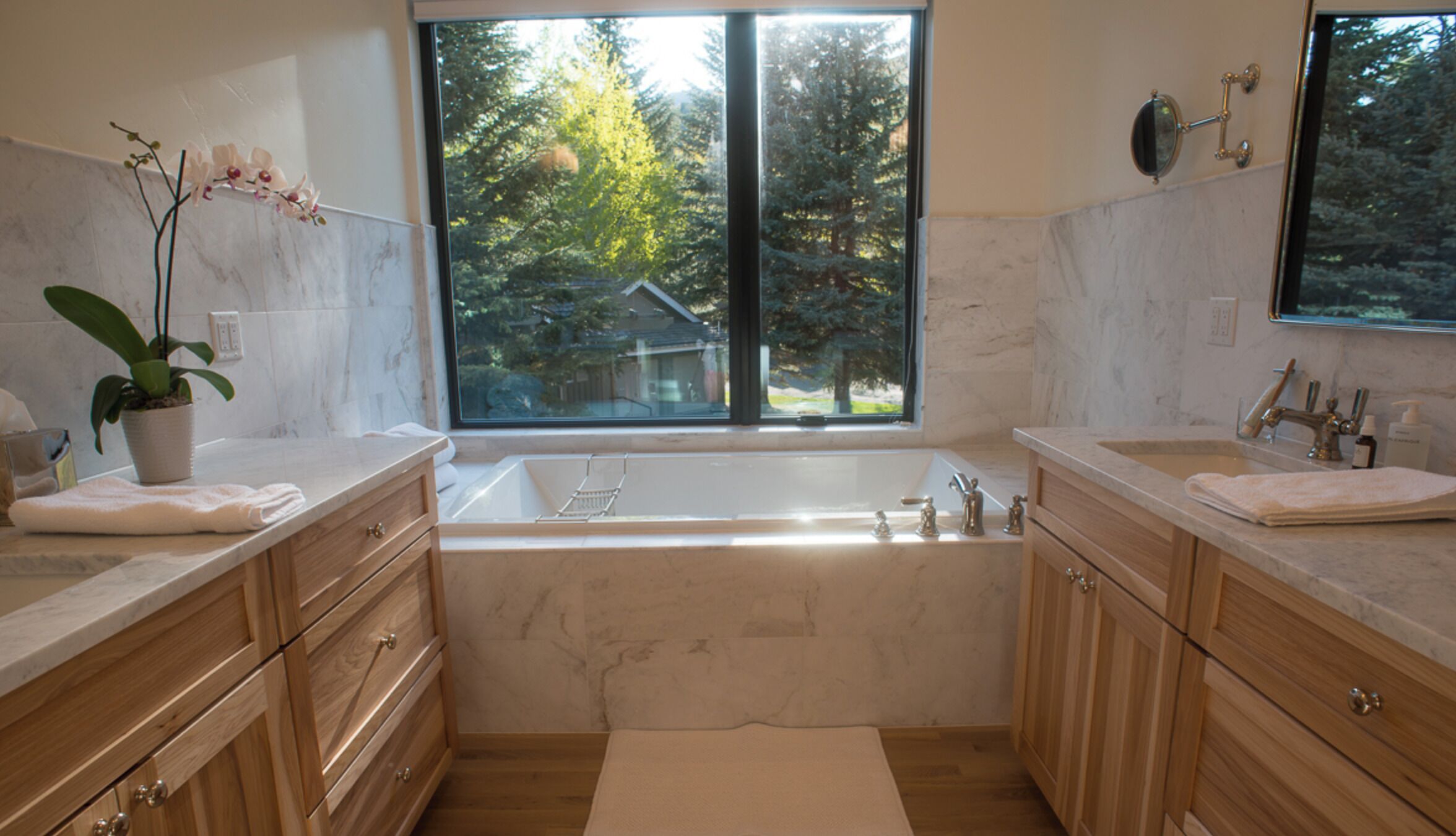 A modern bathroom with a large window, a bathtub, and wooden cabinets.