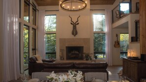 A spacious living room with a fireplace, leather sofa, dining table, and large windows. - Beautiful Mountain Modern Home with well equipped kitchen. Perfect for families. (Ketchum)