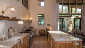A modern kitchen with wooden cabinets, a large island, and a view of the outdoors through large windows. - Beautiful Mountain Modern Home with well equipped kitchen. Perfect for families. (Ketchum)