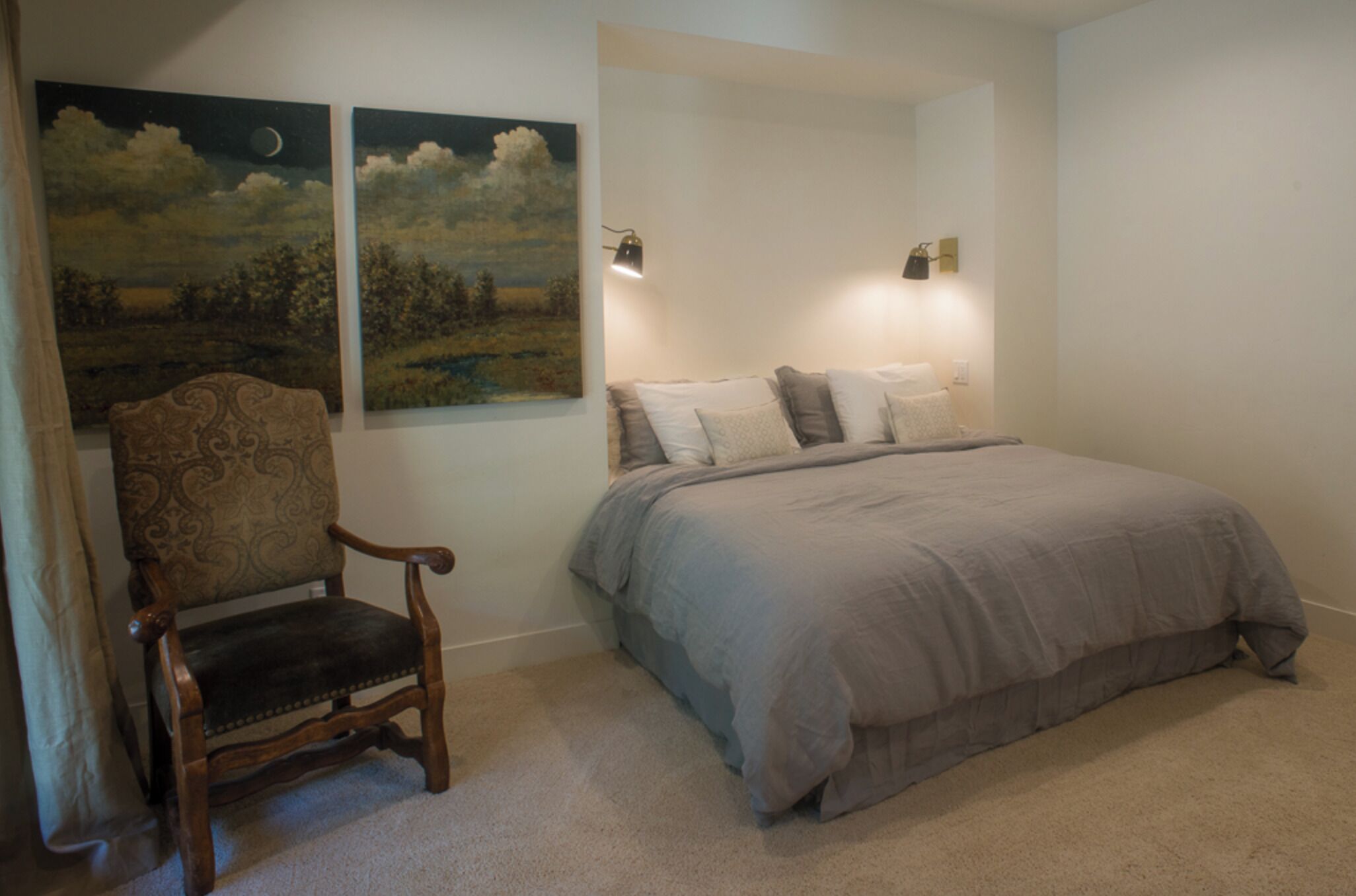 A bedroom with a bed, a chair, and two wall-mounted lamps.