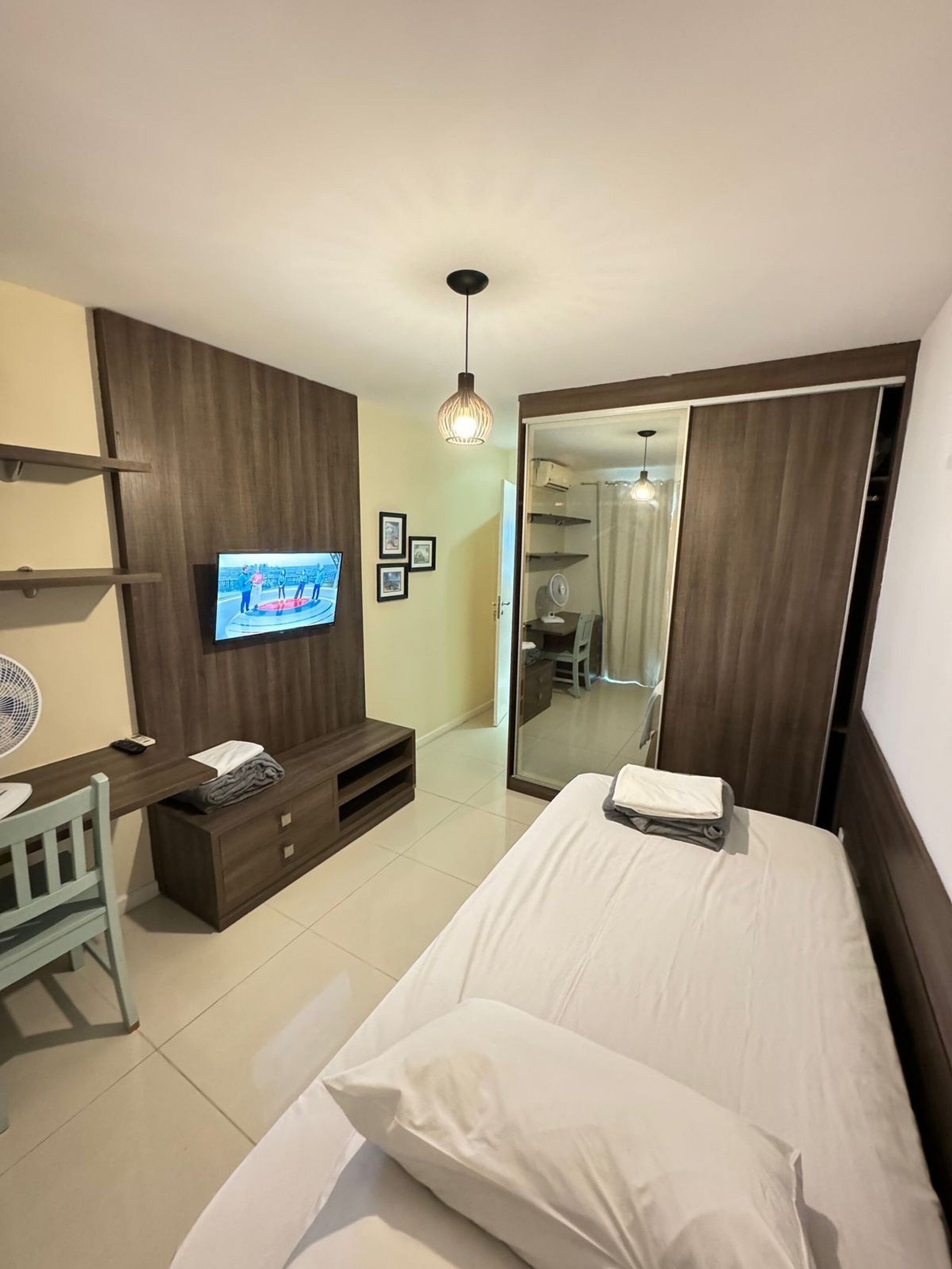 Habitación de hotel con cama, televisión montada en la pared, escritorio con silla, espejo y armario.