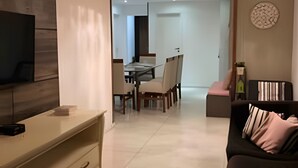 Una sala de estar moderna con un televisor de pantalla plana, un sofá, un comedor con sillas y una araña.