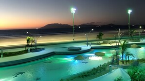Zona de piscina con vistas a la playa y las montañas al atardecer.