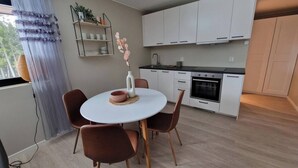 Ett modernt kök med vita skåp, ett runt matbord och bruna stolar.