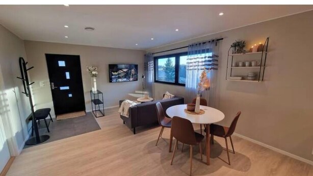 Ett modernt vardagsrum med en matplats, en soffa, en tv och ett fönster med gardiner.