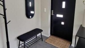 En hall med en svart klädhängare, en bänk, en svart dörr med fyrkantiga fönster och ett litet bord med en växt.