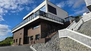 A modern building with a flat roof, large windows, and a staircase leading to a balcony.