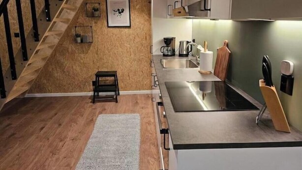 A modern kitchen with a wooden staircase, stainless steel appliances, and a small rug on the floor.