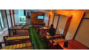 Un restaurante pequeño y acogedor con mesas y sillas de madera, una pantalla de televisión y una alfombra verde.