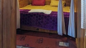 Una habitación acogedora con techo y paredes de madera, una cama con edredón púrpura y amarillo, y cortinas en las ventanas.