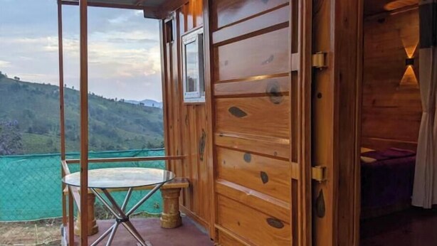 Una cabaña de madera con una mesa de vidrio y vistas a colinas verdes.