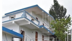 Ein mehrstöckiges Gebäude mit blau-weißer Fassade, einer Treppe, die zu den oberen Stockwerken führt, und einem kleinen Gartenbereich mit einem Kiesweg.