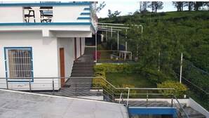 A building with a staircase leading to a balcony, surrounded by greenery. - Diamond hill view cottage (Ooty)