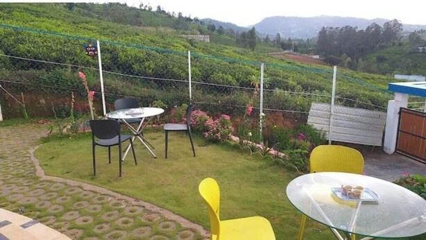 Un patio con mesa y sillas de vidrio, rodeado de un jardín exuberante y vistas a un viñedo.