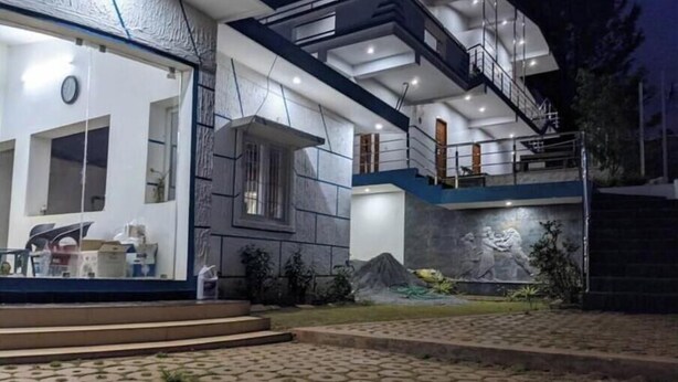 Una casa moderna de dos pisos con una escalera visible, un ventanal grande y un mural en la pared exterior.