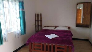A bedroom with a wooden bed, a purple bedspread, a window with curtains, and a wooden wardrobe. - Kathiresan's Diamond hill view cottage (Ooty)
