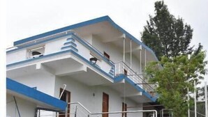 A multi-story building with a blue and white exterior, a staircase leading to the upper floors, and a small garden area with a stone pathway. - Kathiresan's Diamond hill view cottage (Ooty)