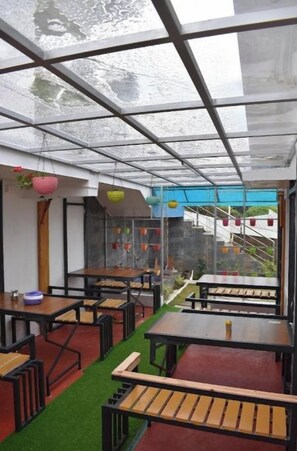 An indoor dining area with tables and benches, a glass ceiling, and a view of the outside. - Kathiresan's Diamond hill view cottage (Ooty)