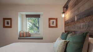 A bedroom with a bed, a window with a view, and a wooden headboard. - Nestled In Nature Home - Pet-Friendly, Acreage (Austin)