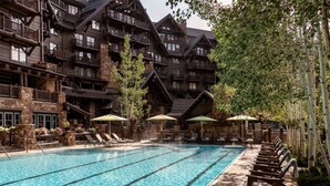 Ein Poolbereich mit Liegestühlen und Sonnenschirmen, umgeben von einem Holzgebäude mit mehreren Balkonen.