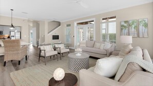 A spacious living room with a high ceiling fan, a dining area with wicker chairs, a kitchen with modern appliances, and a staircase leading to another level.