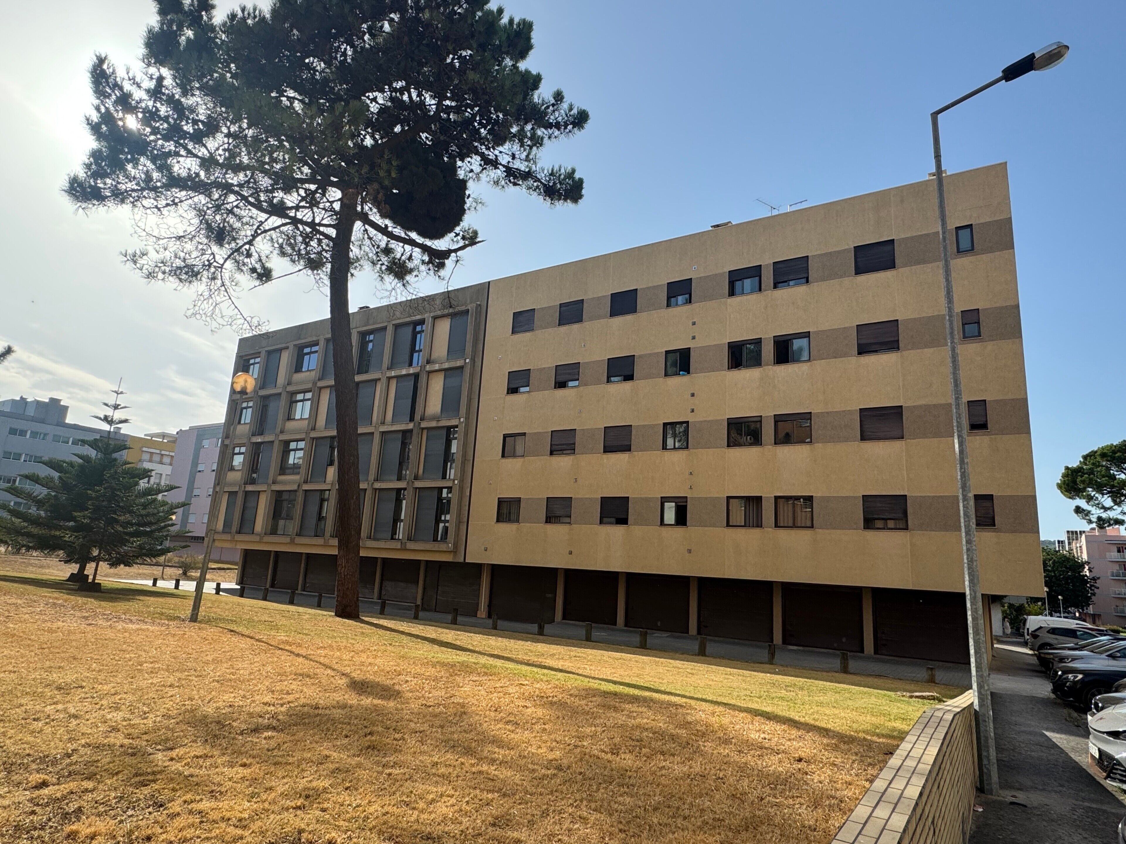 Un edificio a più piani con facciata lineare, molte finestre e un'area di parcheggio con auto.