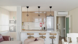 Uma cozinha moderna com uma ilha central, banquetas de bar e uma  área de refeições com uma mesa e cadeiras brancas.