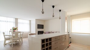 Uma cozinha moderna com ilha central, área de jantar com mesa e cadeiras brancas, e uma grande janela que proporciona iluminação natural.