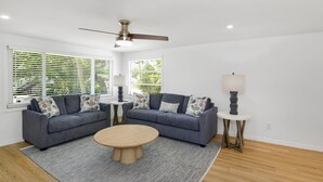 Ein Wohnzimmer mit zwei grauen Sofas, einem runden Couchtisch, einem Deckenventilator und einer Lampe auf einem Beistelltisch.