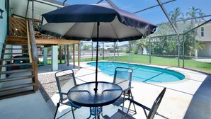 Ein überdachter Außenbereich mit Pool, Tisch und Stühlen sowie einem Sonnenschirm.