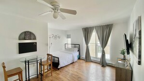 A bedroom with a bed, a desk with a chair, a ceiling fan, and a window with curtains. - Studio urbain à Ville-Marie – 309, emplacement central à Montréal (Montréal)