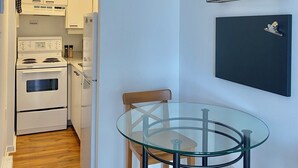 A compact kitchen with white appliances, a glass table, and a wall-mounted coffee menu. - Studio urbain à Ville-Marie – 309, emplacement central à Montréal (Montréal)