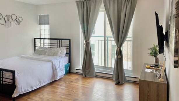 A bedroom with a bed, curtains, a window, a TV, and a small table with a plant. - Studio urbain à Ville-Marie – 309, emplacement central à Montréal (Montréal)