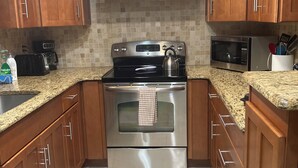 A kitchen with wooden cabinets, a stainless steel stove, a microwave, and a tiled backsplash.