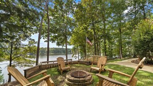 Terraza junto al lago con sillas Adirondack de madera y una chimenea, rodeada de árboles y vistas al lago.