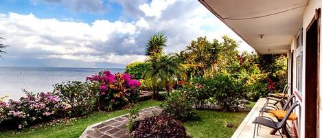 Un balcon offrant une vue sur la mer, entouré d’une végétation luxuriante et de fleurs aux couleurs vives.