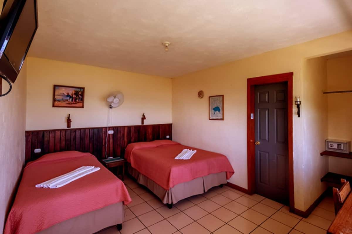A hotel room with two beds, a fan, a door, and a small table with a radio.